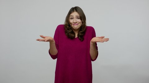 Don't know answer. Confused clueless uncertain brunette woman in pullover spreading hands in questioning gesture, looking puzzled and embarrassed. indoor studio shot isolated on gray background