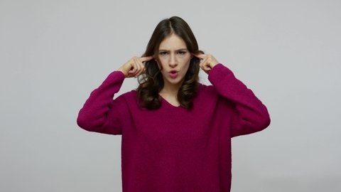 Irritated brunette woman in pullover closing ears with fingers and saying no, ignoring conflict, not listening to annoying talk or someone opinion. indoor studio shot isolated on gray background