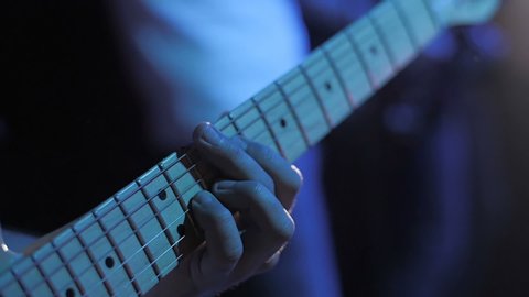 Guitarist performs on stage. Performing in slow motion. Closeup guitar view. Metal concert. Rock gig. Guitar strings. Rock music band. Music player. Electric guitar. Young music artist. Grunge concert