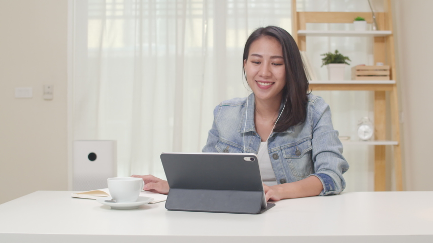 Asia freelance business women casual wear using tablet working call video conference with customer in workplace in living room at home. Happy young Asian girl relax sitting on desk do job in internet. Royalty-Free Stock Footage #1046581954