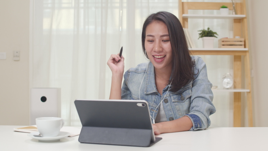 Asia freelance business women casual wear using tablet working call video conference with customer in workplace in living room at home. Happy young Asian girl relax sitting on desk do job in internet. | Shutterstock HD Video #1046581954