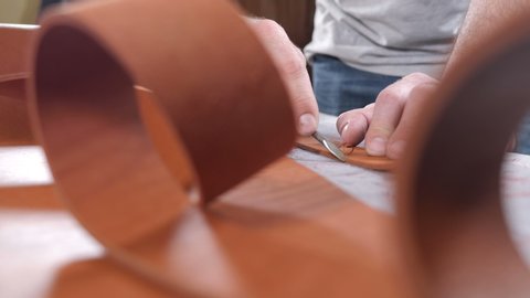Craftsman work with big peace of leather at workshop. Male leather worker cuts off extra piece of material with utility knife. Cutting leather for belt. Close up 4k