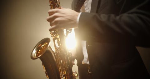 A saxophonist wearing a suit performing a solo on stage, spotted and silhouetted by light - arts, jazz music concept 4k footage