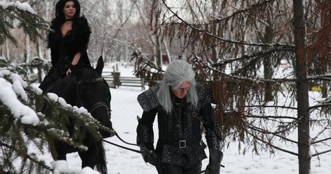 Dnipro, Ukraine - February 06, 2020: Cosplayer in image of a characters Geralt of Rivia walks next to Yennefer of Vengerberg riding a horse from the game or film The Witcher in snowy winter forest.