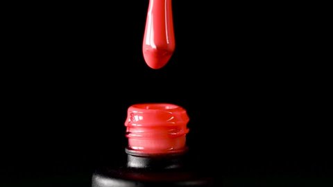 A drop of nail polish drips into an open bottle on a black background. Advertising gel-lacquer for nails of bright color. Slow drop drops of nail gel varnish into the bubble.