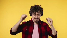 Handsome happy european man with beard in red shirt smiling and dancing isolated on yellow background. Guy in headphones listening to music. Lifestyle concept. Slow motion.