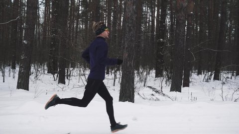 Running Man In Sportswear Workout Before Triathlon. Runner Man Running Winter Forest Snow Trail. Winter Sports And Recreation Concept. Young Man Training Jogging Outdoor In Winter. 