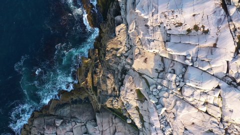 Aerial Drone view of the coastline at Peggy's Cove lighthouse in Nova Scotia, Canada. The drone is capturing the texture of the white rock with the waves crashing against it.