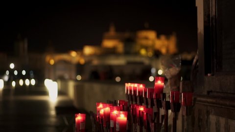 Pan shot right to left of Saint Raphael statue at night on the Roman Bridge of Cordoba. View of Mosque-cathedral, Catedral de Cordoba behind candels on the roman bridge