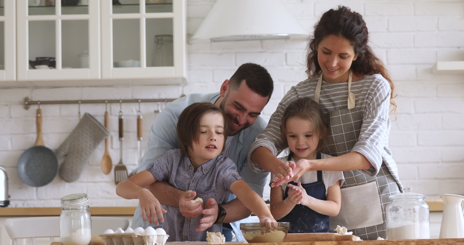 Happy full family kneading dough, having fun together at home. Smiling married couple playing with joyful little kids siblings while making homemade bakery, enjoying spending free time in kitchen. Royalty-Free Stock Footage #1046602015