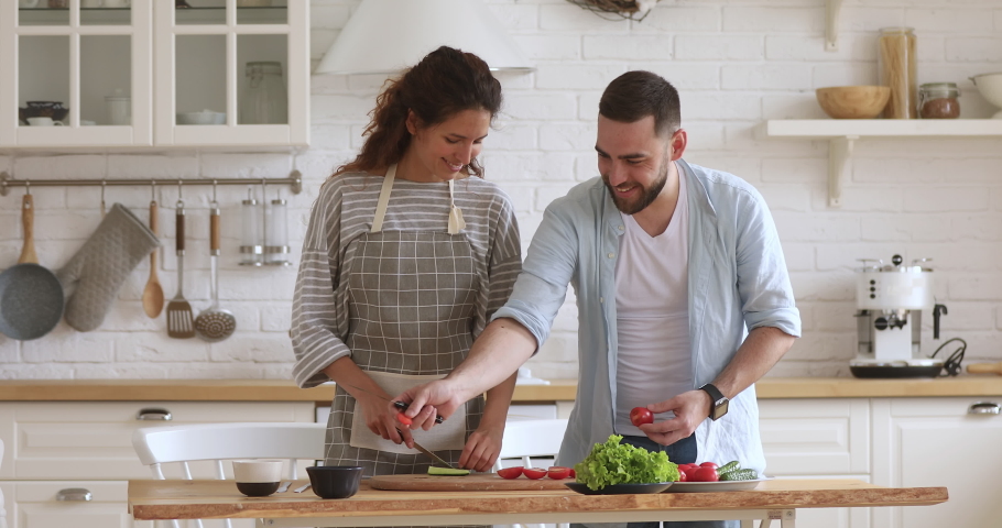 Happy attractive woman feeding husband while cooking together at modern kitchen. Smiling family couple laughing, enjoying preparing healthy vegetarian food salad meal for romantic dinner at home. Royalty-Free Stock Footage #1046602051