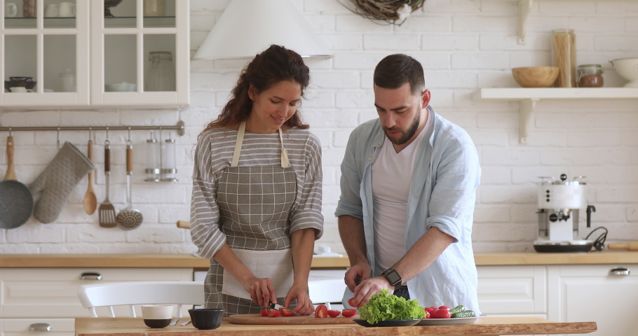 Happy attractive woman feeding husband while cooking together at modern kitchen. Smiling family couple laughing, enjoying preparing healthy vegetarian food salad meal for romantic dinner at home. Royalty-Free Stock Footage #1046602051
