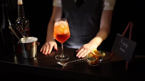 Barmaid decorating Aperol spritz cocktail, adding a slice of orange into a wine glass filled with ice