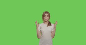 worried girl standing with fingers crossed for good luck and wins isolated over green background. Young woman praying on chroma key. 4k raw video footage slow motion 60 fps