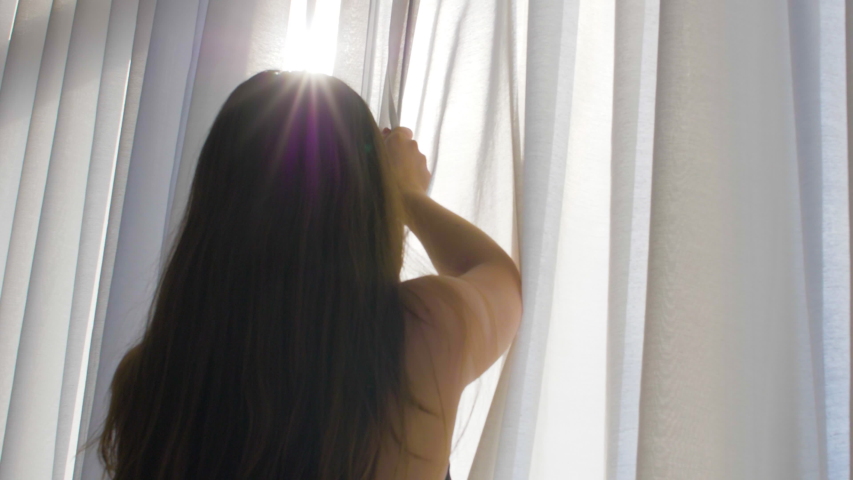 A young attractive female approaches a window, and opens curtains. Then, you can see a city panorama view.
All in slowmotion, 4K at 60fps.

Other tags could be window, woman, morning, curtains | Shutterstock HD Video #1046608102