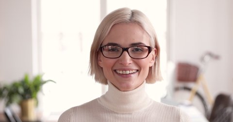Smiling confident young adult blonde businesswoman manager professional wear glasses looking at camera in corporate office, happy smart millennial female model worker manager close up face portrait