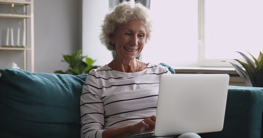 Happy excited middle aged grandma looking at laptop screen, communicating with grownup children online. Older client making purchases buying goods in internet store, easy technology usage concept. Royalty-Free Stock Footage #1046611597