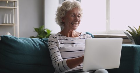 Happy excited middle aged grandma looking at laptop screen, communicating with grownup children online. Older client making purchases buying goods in internet store, easy technology usage concept.