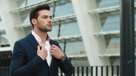 Portrait confident businessman walking in stylish suit outdoors. Thoughtful man looking away outdoors at city. Young business man buttoning elegant suit at street.