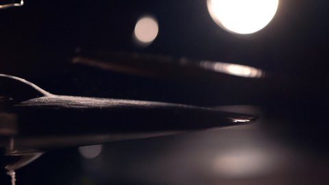 Playing hi-hat musical instrument using two sticks in slow motion on dark background with lights of spotlight, closeup side view. Drum cymbal vibration. Drumsticks hitting on metal crash cymbal