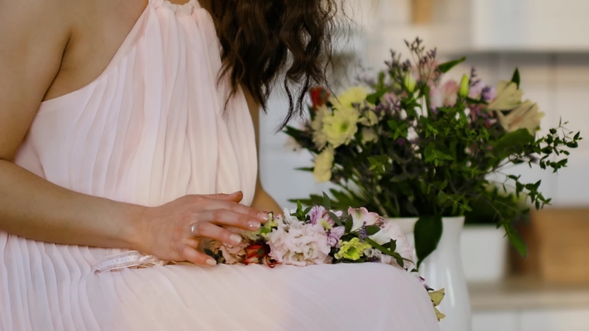 Portrait of a stunningly beautiful Asian young woman in a delicate pink dress with spring flowers in her hands. Woman enjoying flowers in a bright room under the morning sun. Slow motion