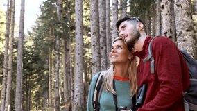 Video of two travel hikers with backpack looking the landscape while woman pointing something in the forest.