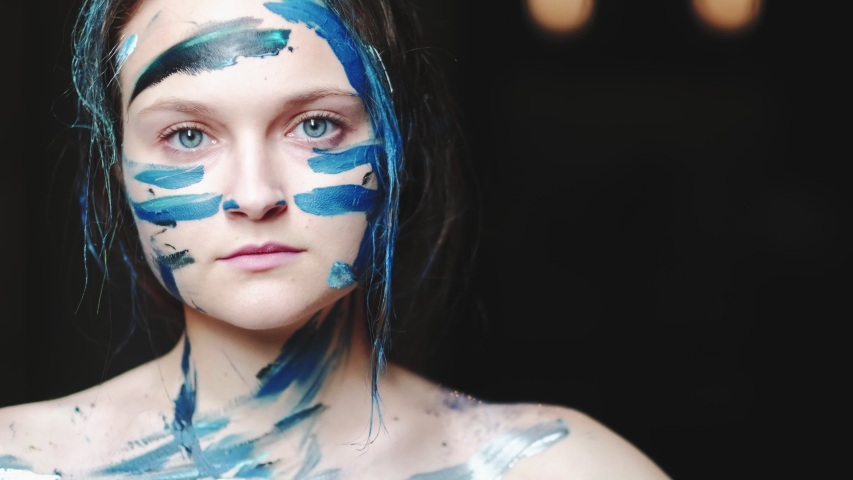 Art obsession. Emotion expression. Woman smearing blue paint over face neck bare shoulders.