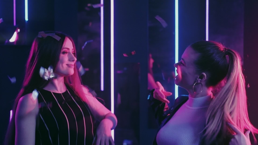 Neon girls. Fun celebration. Amused female friends dancing in confetti rain nightclub purple glow.