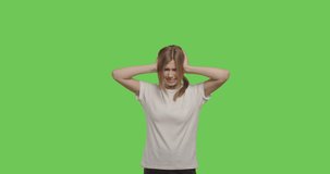 young woman puts her hands in her hair and shows a painedisolated over green background, stressed expression. Girl close ears on chroma key . 4k raw video footage slow motion 60 fps