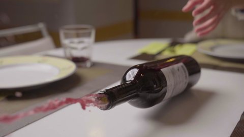 Slow motion close up shot of bottle of red wine opening and overturned on white marble table set. Drink falling down, red wine spilling and spreading on the dinner table. Stop drinking alcoholism icon