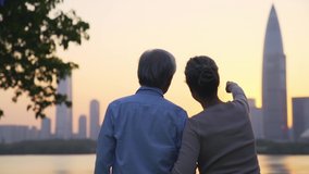 rear view of asian senior couple looking at sunset on city skyline by a river - Powered by Shutterstock - Get 15% off with code: PIKWIZARD15