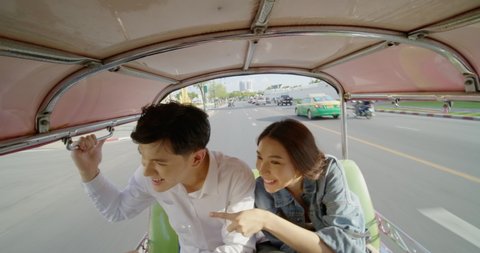 Asian couple travelling inside a Tuk Tuk vehicle in the street at Bangkok city. Sweet couple travel in holiday trip.