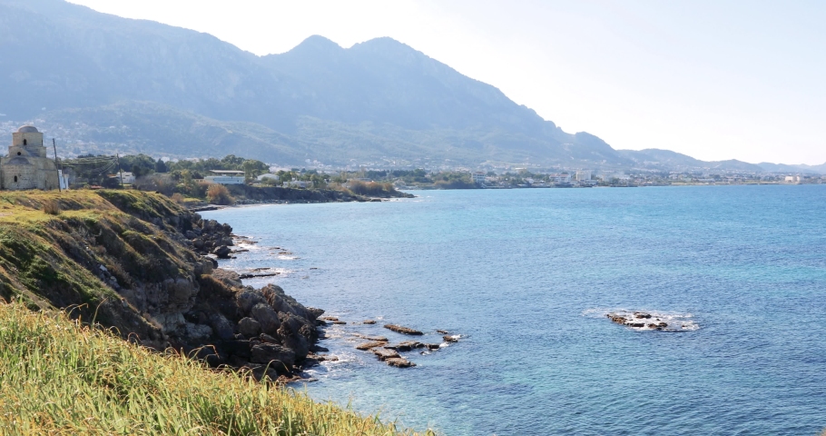Coastline of northern island Cyprus with Kyrenia mountains and ruins of historic building. Waves crash on rocky shore creating splashes. Scenic marine Mediterranean landscape with natural beauty and r