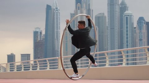 Cyr Wheel artist doing tricks slow motion wearing black and white smart clothes with cityscape background of Dubai during sunset