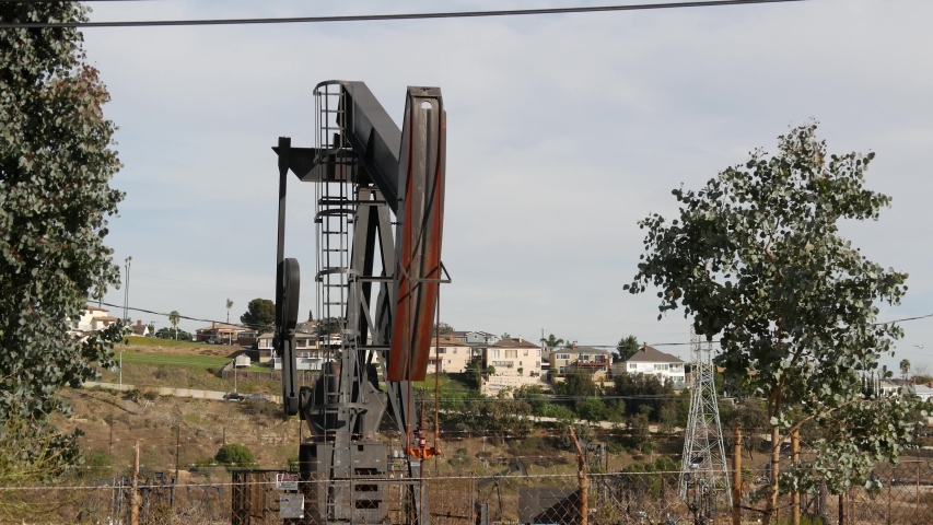 Industrial urban landscape. La Brea Inglewood in Los Angeles. Well pump jack operating behind the fence. Drilling rig extract crude oil. Oil mining machine with working piston. Oil and gas industry.