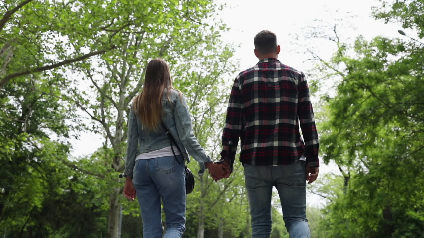 A young couple holding hands walks along the alley in a spring park.