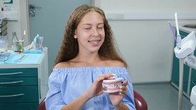 Smiling girl with orthopedic dental braces in dental chair. Healthcare, Dental Health and Dentistry concept. Happy Young Caucasian girl Looking at Camera Posing on dental office Background for Video