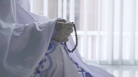 Close up of old woman hands holding beads during praying to the Allah and sitting near the window. Shot in 4k resolution