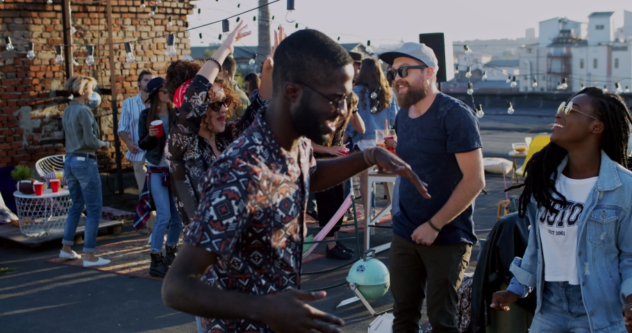 African American young joyful and stylish couple dancing together among multiethnic people at the rooftop party at day. Outdoor.