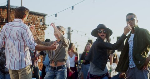 Young mixed-races men and women dancing cheerfully at the celebration of big holiday on the rooftop during a party. Outdoors.