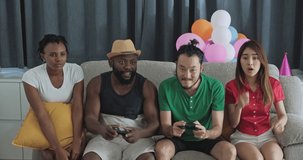 Friends playing console game together in house party, team won big. Summer break party among friends. Mixed race asian, thai, chinese, African american. In living room party.