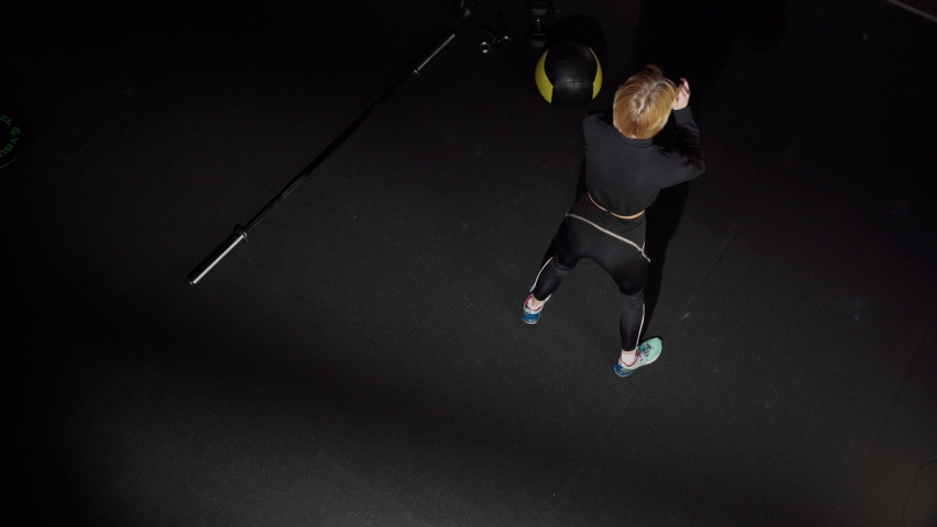 High angle back view of fit young woman in black sportswear doing squats and stretching leg muscles during cross training in gym
