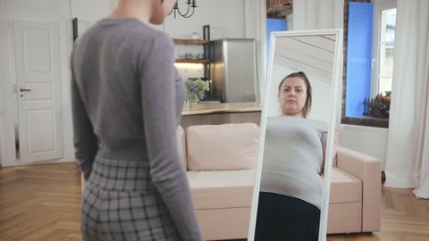 Slim woman seeing herself fat in mirror. Anorexia, bulimia, eating disorder concept. Insecure skinny woman looking in mirror and seeing herself as overweight.