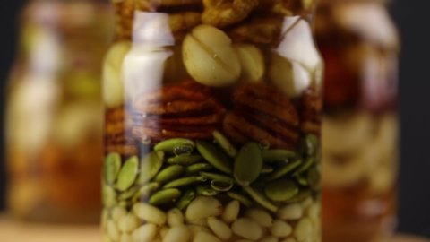 Glass jars with nuts and seeds in honey rotate clockwise, side view, close-up