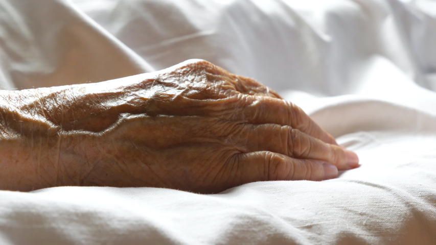 Worried man taking and gently stroking hand of his sick mother showing care or love. Son comforting wrinkled arm of elderly mom lying at bed. Guy giving support to his old parent. Side view Close up | Shutterstock HD Video #1046683780