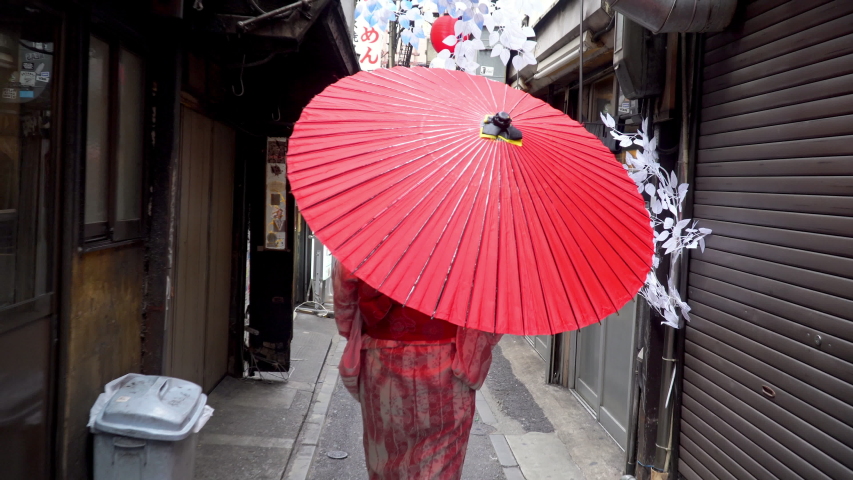 Beautiful Asian woman tourism in pink traditional japanese kimono dress holding red umbrella walking in city street with happiness. Smiling kimono girl enjoy outdoor lifestyle activity travel in Japan