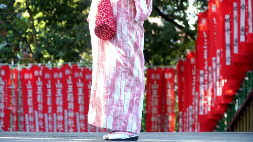4K Happy young beautiful Asian woman girls with smiling face wearing pink traditional Japanese kimono dress holding red umbrella standing at Torii Gate in autumn at Japanese temple.