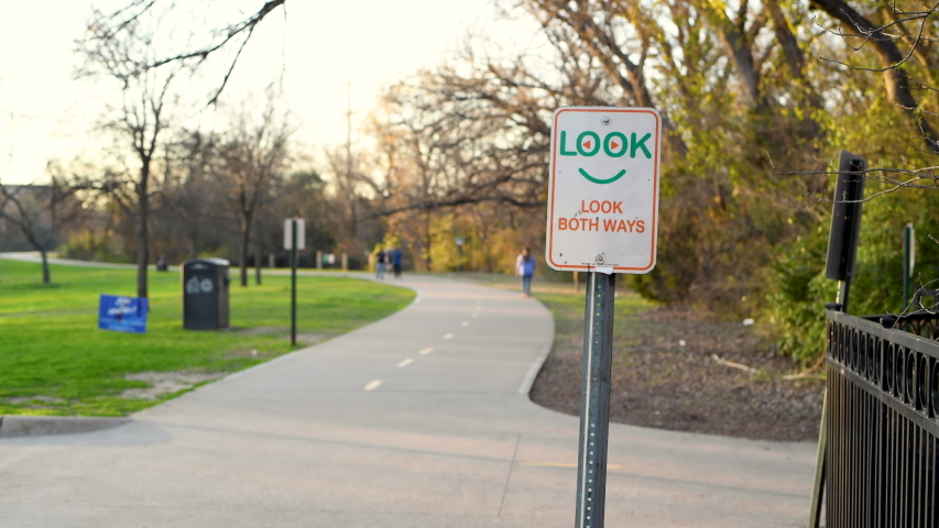 Cyclist and joggers pass a sign that reads look both ways on the White Rock Lake bike and jogging path in Dallas Texas