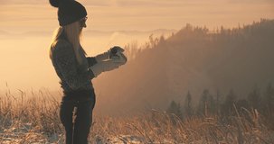 Woman traveler drinking hot tea and relaxing in the forest on sunny winter day. Beautiful mountain landscape view. 4K slow motion video.
