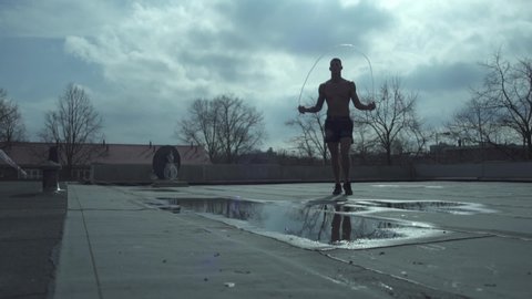 Netherlands, Amsterdam 26.03.2016  A fighter or athlete jumps on a skipping rope.On the roof. On the street by the puddle